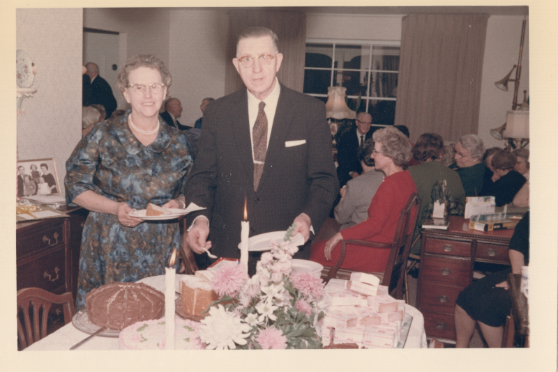 A man and woman smile while grabbing pieces of cake