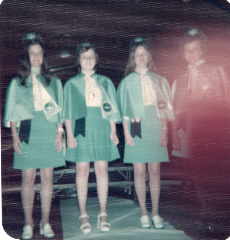 Three missionettes stand on stage with an adult leader