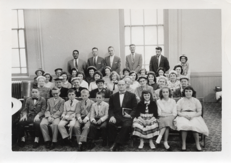 Men, women, and children sit together in pews for a group photograph