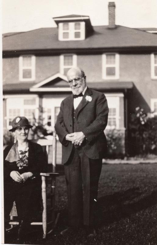 A man and a woman in a chair smile for a portrait outside of a home