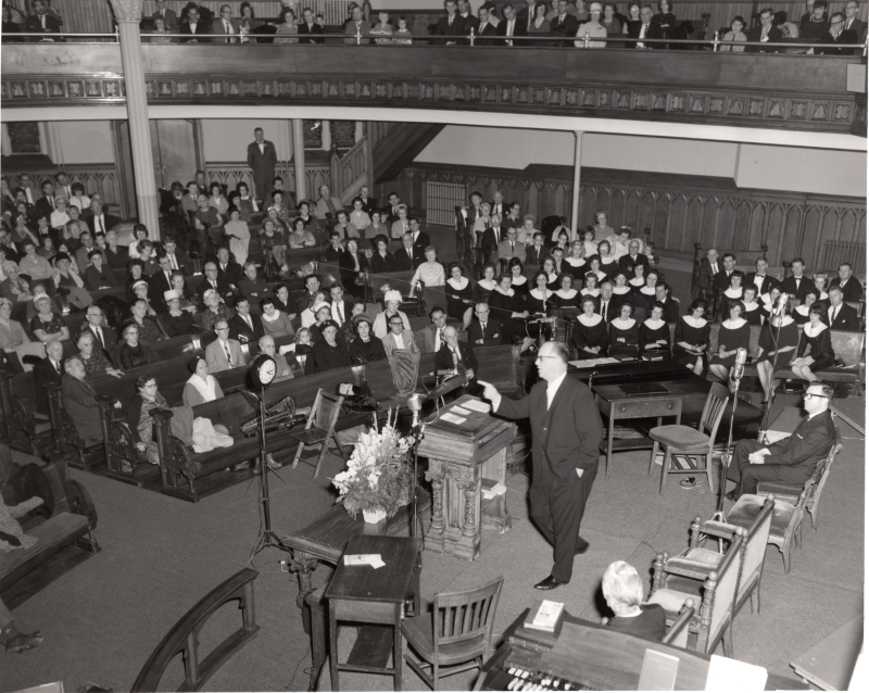 A man leads the Revivaltime broadcast in front of a large congregation