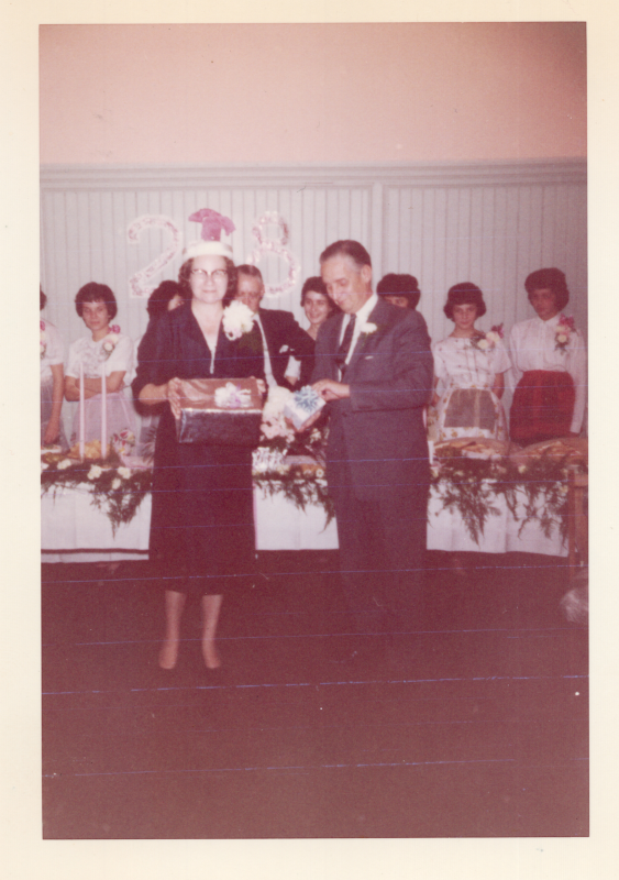 Pastor and Mrs. Roberson are presented with presents in front of a table of holiday food and the number "28" on the wall