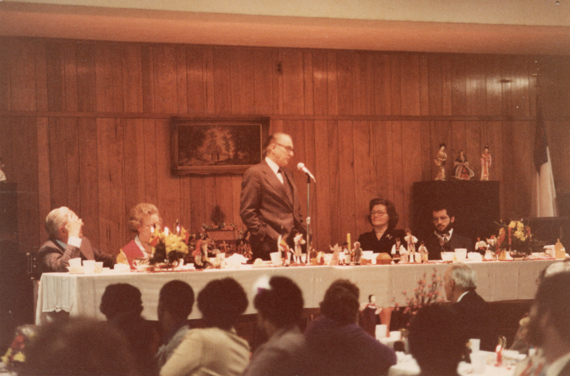 A man speaks into a microphone to a room of dining congregants