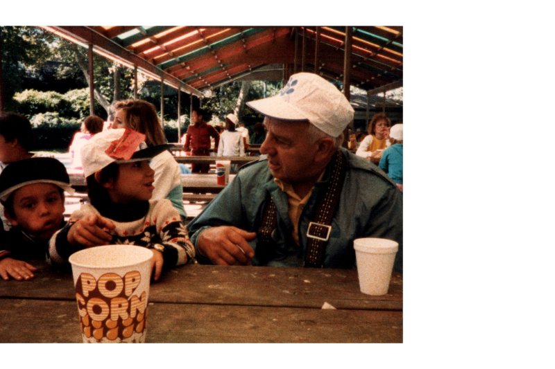 Two children eat popcorn with an older man at the zoo