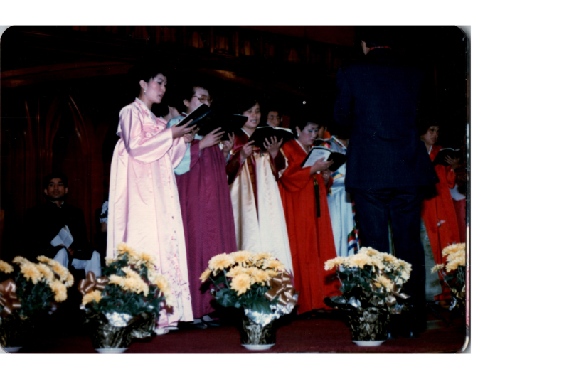 A group of women in Hanbok lead a song from a hymnal on stage in the sanctuary