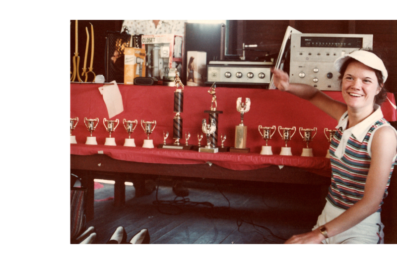 A woman sits with trophies and prizes