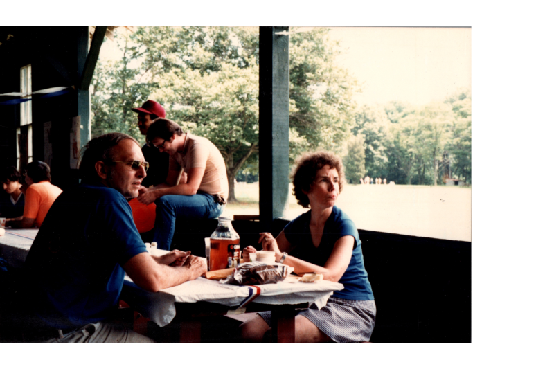 People sit around picnic tables in a pavillion
