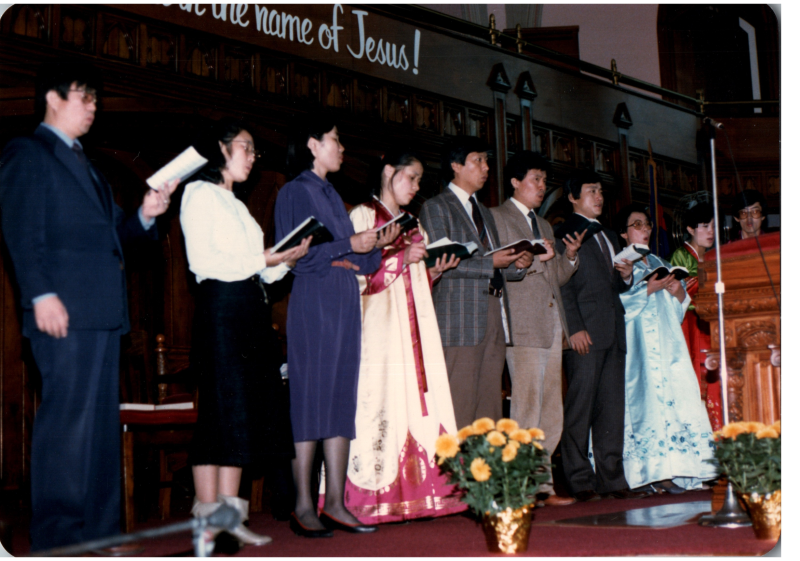 A group with several people dressed in traditional Korean clothing lead a song from hymnals