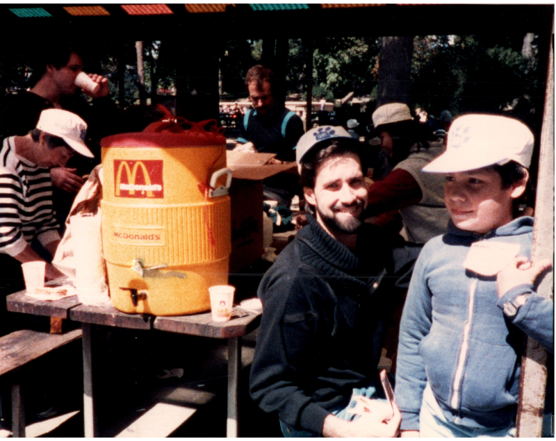 A man smiles with a boy under a pavillion with refreshments