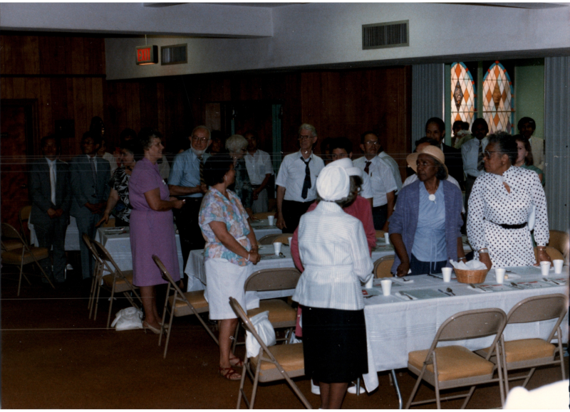 Congregants stand together around dinner tables