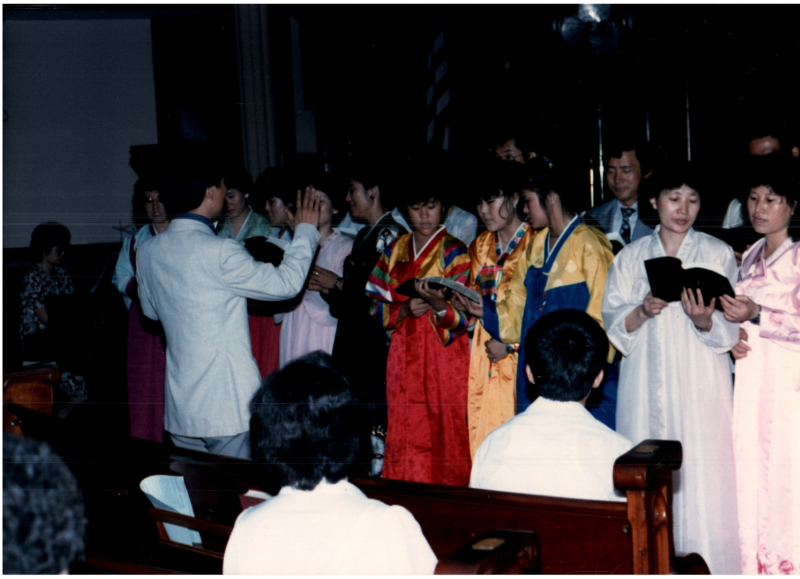 Women in hanboks lead a song from a hymnal