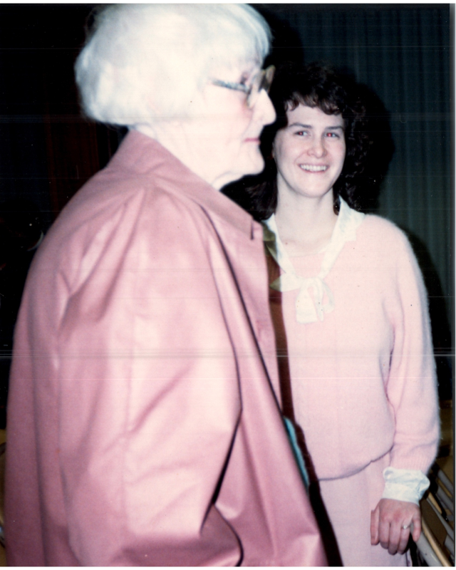 A woman smiles for a picture with an older woman in the foreground
